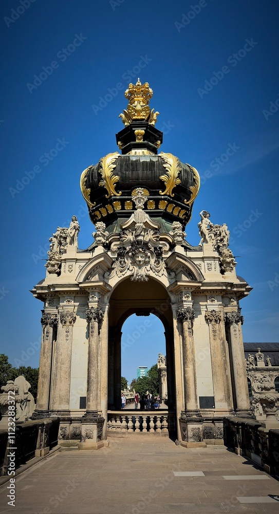 Obraz premium a dome on which rises a crown decorated with gold elements. The arch is surrounded by sculptures and decorative details such as stucco, bas-reliefs and columns. The background consists of a clear blue