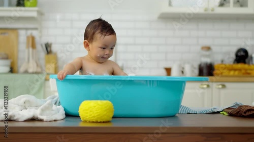 Asian baby taking a bath in a blue tub at home.
