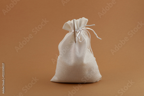 White burlap bag on beige background, close-up. A sharp awl sticks out of the bag. Creative visualization of proverbs- You can't hide an awl in a bag. Murder will out.