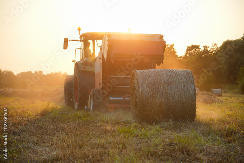 Tractor baling hay in a field at sunset. Modern agricultural machinery for efficient haymaking and livestock feed production, farmer work and agricultural productivity