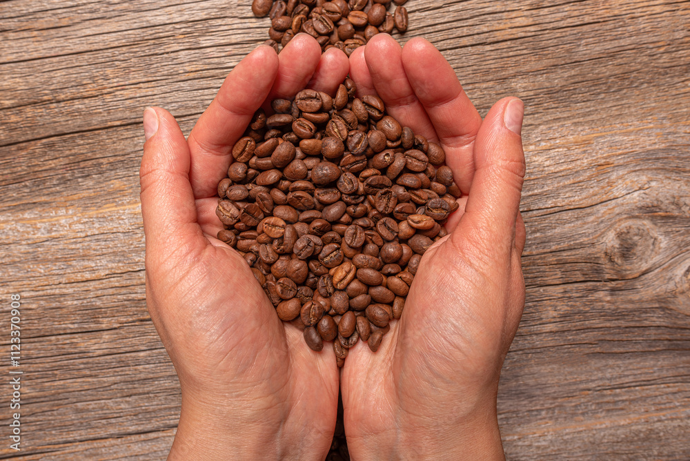 Coffee beans in female hands on wooden background.