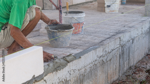 Construction of a lightweight brick wall by a male worker Use a trowel to scoop cement onto the alignment line.