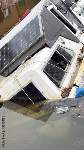 Vertical shot. Close up of sunken boat in the canal water, loose rubbish floating, environmental damage.