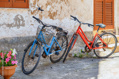 One red and one blue retro bike parked in front of  old building in Italy.