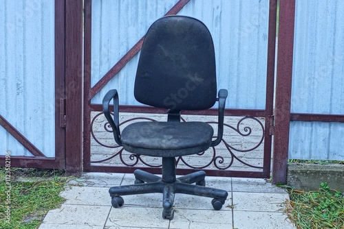 one  comfortable simple  empty office dirty old swivel modern plastic with armrests black round soft chair stands on gray tiles near iron gate during daytime outside photo