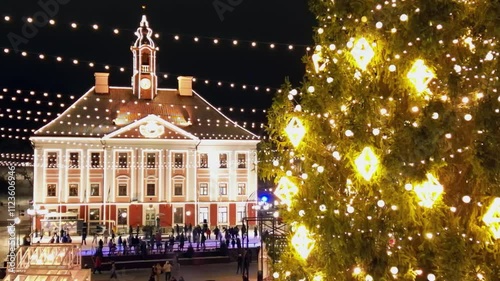 Christmas market in the center of Tartu Estonia, In the middle of the main square, there is a big Christmas tree decorated with bright yellow lights and an ice skating rink, people enjoy hanging out