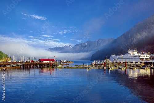 Horseshoe Bay Ferry Terminal and Marina, West Vancouver, boats and yachts moored against a backdrop of snow-capped mountain range, fog on the water and a beautiful cloudy sky