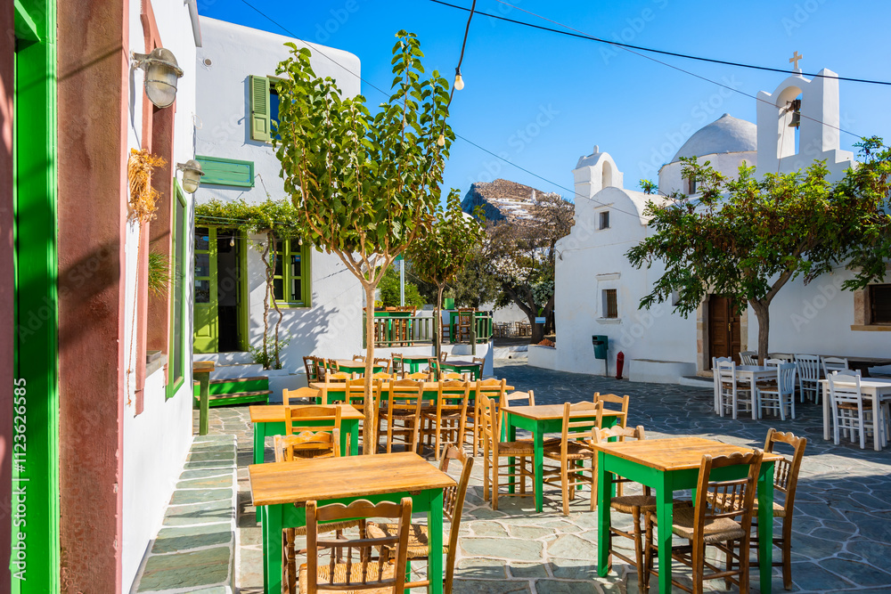 Obraz premium Square with white typical Greek church and tavern restaurant tables and chairs in Chora village, Folegandros island, Cyclades, Greece