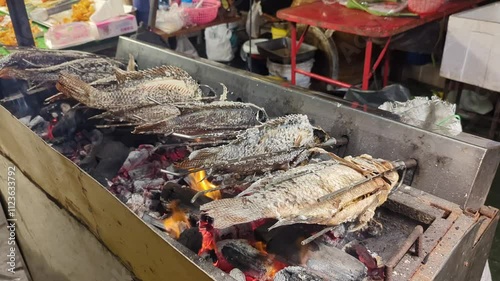 Cooking grilled and skewered fish,rotating slowly, over a burning barbecue,Hua Hin,Thailand.