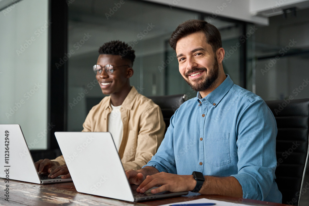 Fototapeta premium Portrait of professional young happy business man worker software development engineer working with colleague developer in office. Diverse employees using laptops computer technology at work.