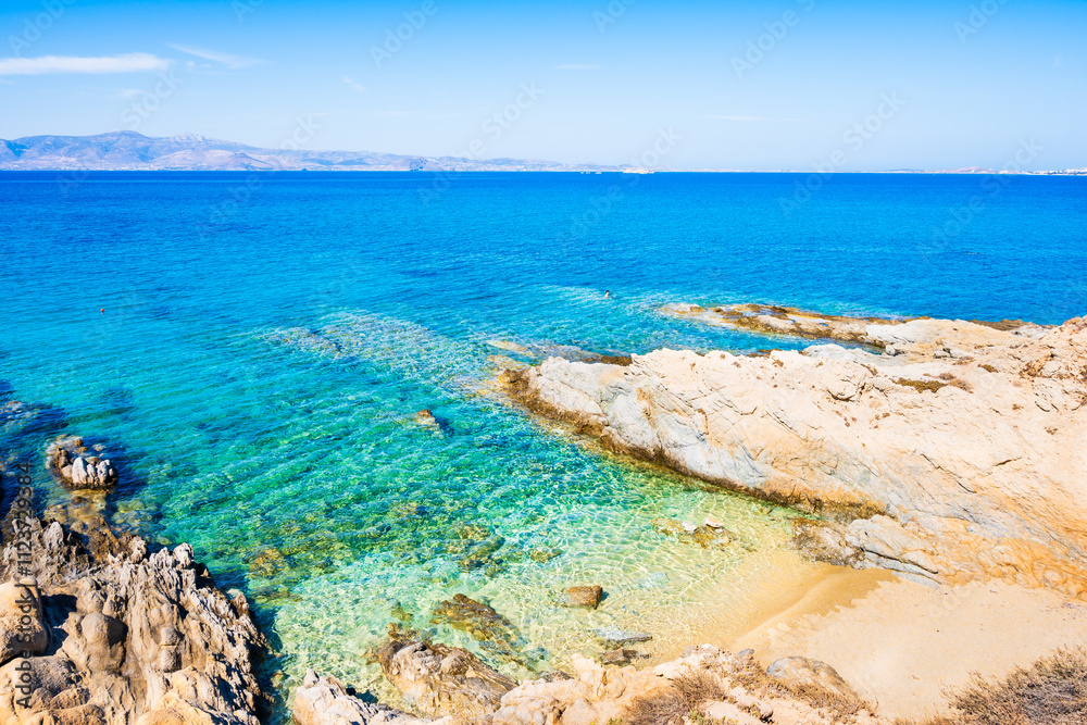 Rocks and stones on idyllic sandy beach of Orkos bay and calm crystal clear azure sea water, Naxos island, Cyclades, Greece