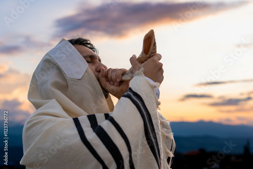 Young Jewish man blowing the shofar at sunset to celebrate the beginning of the Hebrew month or Rosh Jodesh