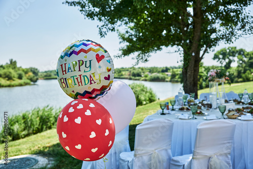 Birthday party outdoor celebration lake balloons white tablecloths chairs decorated nature scenic view festive atmosphere.