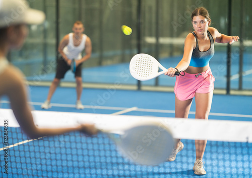 Young woman and young man in doubles play against adult woman on tennis court photo