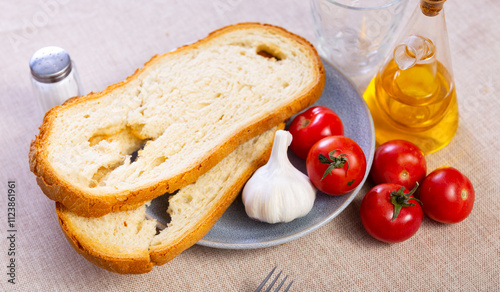 Crispy toasted white bread slices, fresh ripe tomatoes, spicy garlic on plates and carafe of olive oil served on table. Ingredients for traditional Catalan tapas Pan con tomate..