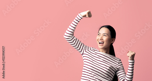 Overjoyed Young Asian Woman Celebrating Success With Raised Fists, Euphoric Korean Lady Shouting Yes, Emotionally Reacting To Win Or Good News, Standing Isolated Over Pink Background, Copy Space photo