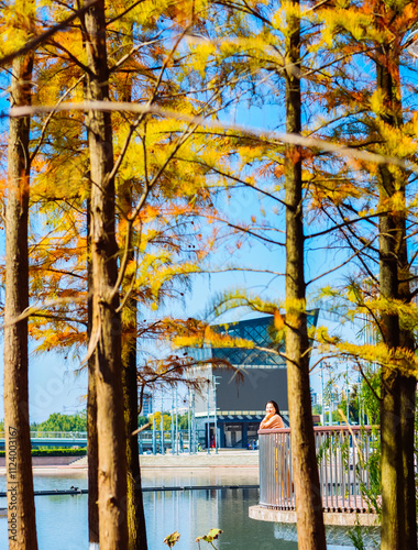 One Asian woman enjoying beautiful landscape of golden autumn season at Yinzhou Park, with white lighthouse and redwood trees in Ningbo, Zhejiang, China