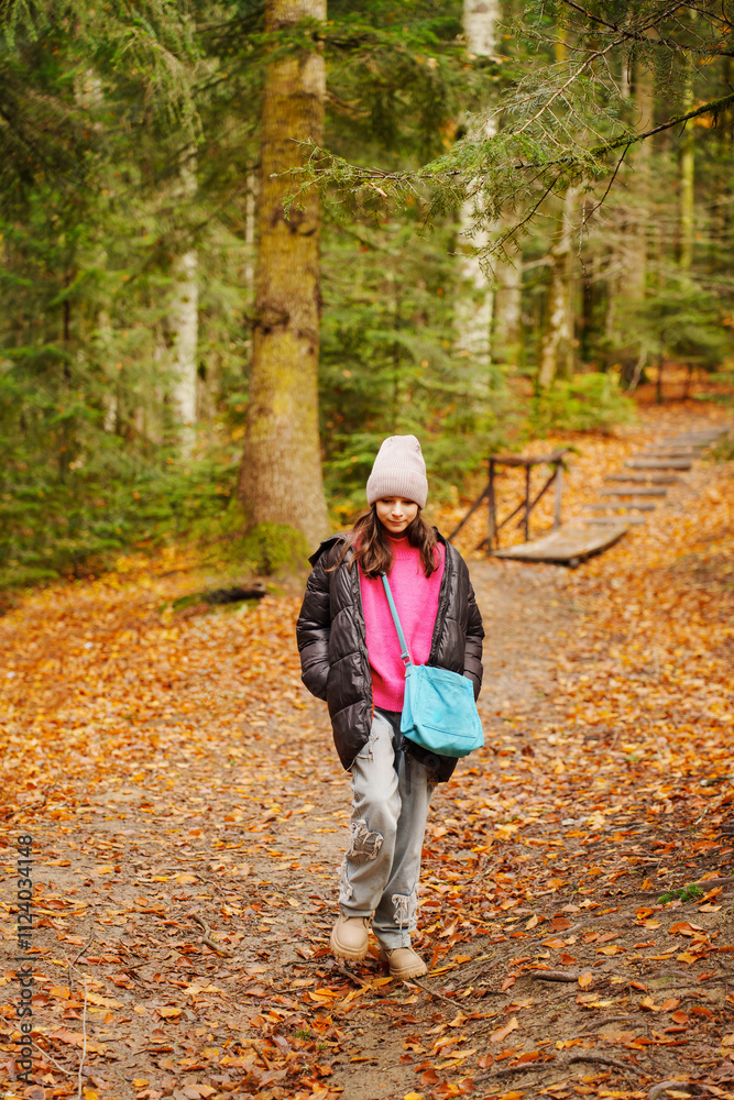 Fototapeta premium a teenage girl in a black jacket and hat on a path in an autumn forest.