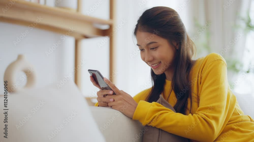 Happy young asian woman relax on comfortable couch at home texting messaging on smartphone, smiling girl use cellphone chatting, online shopping at home, video call communication Happy young asian woman relax on comfortable couch at home texting messaging on smartphone, smiling girl use cellphone chatting, online shopping at home, video call communication