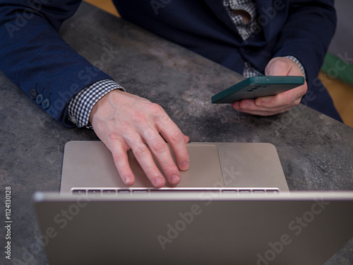 Businessman working remotely at modern office desk, managing tasks on laptop and holding smartphone. Businessman ensures effective communication and productivity Concept of remote work.