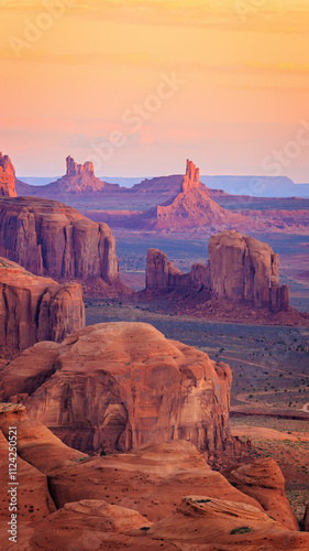 Golden sunrise paints the towering sandstone buttes and mesas of Hunts Mesa in Monument Valley tribal park, located on the Arizona-Utah border, creating a serene, otherworldly desert landscape.