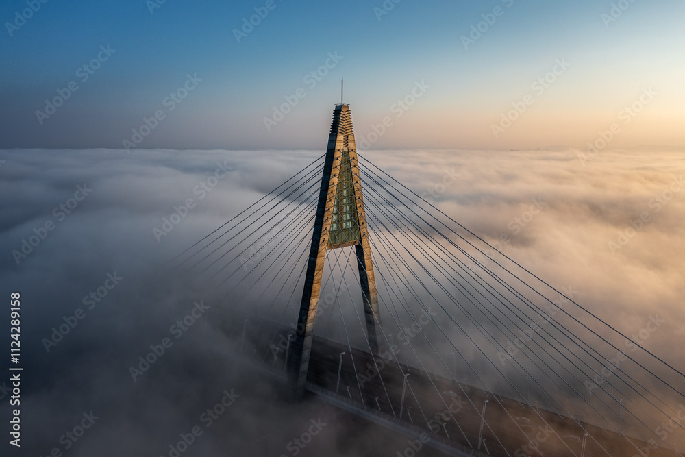 Budapest, Hungary - Aerial view of one of the pillars of the Megyeri Bridge over River Danube covered in heavy autumn fog at sunset with blue and golden sky