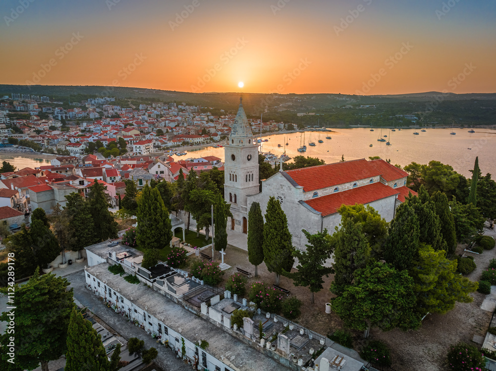 Primosten, Croatia - Aerial view of St. George's Church on Primosten peninsula and old town on a sunny summer morning in Dalmatia, Croatia. Golden sky at sunrise by the Adriatic sea coast