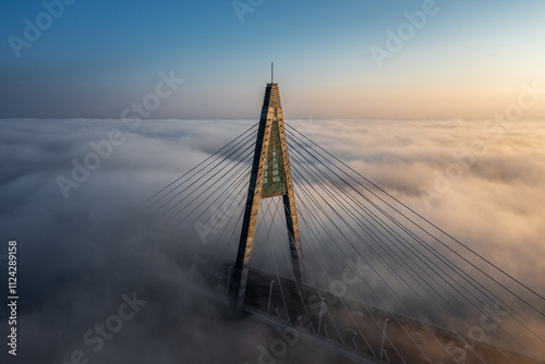 Obraz na płótnie Budapest, Hungary - Aerial view of one of the pillars of the Megyeri Bridge over River Danube covered in heavy autumn fog at sunset with blue and golden sky w salonie