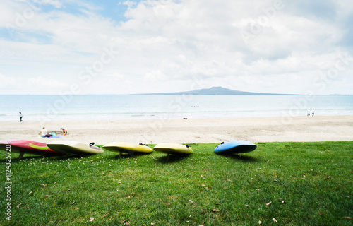 Paddle boards on the beach. Rangitoto Island in the distance. Unrecognizable people and dog walking on Takapuna Beach. Auckland. photo