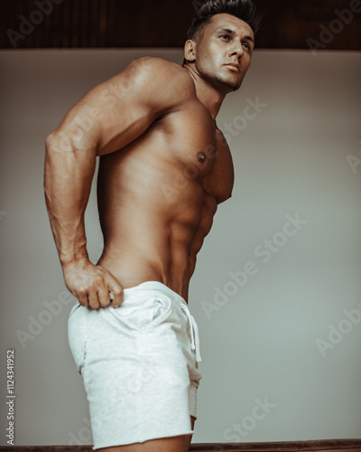 Handsome muscular man in white sports shorts posing in studio. Male fitness model taking off his clothes. Naked brunette with six pack abs.