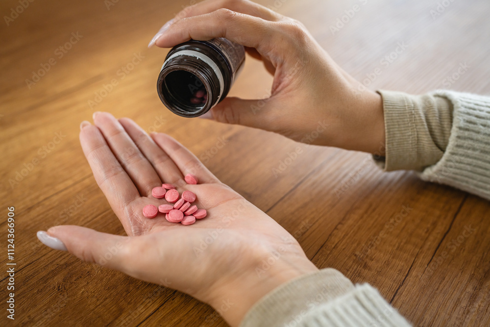 Close-up of a female hand offering pink pills on wooden table surface Close-up of a female hand offering pink pills on wooden table surface