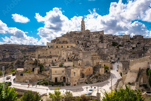 Fototapeta Naklejka Na Ścianę i Meble -  Nestled in the hills, Matera Italy reveals its stunning stone buildings and winding streets under a backdrop of dramatic clouds and blue sky. Experience the charm and history of this ancient city.