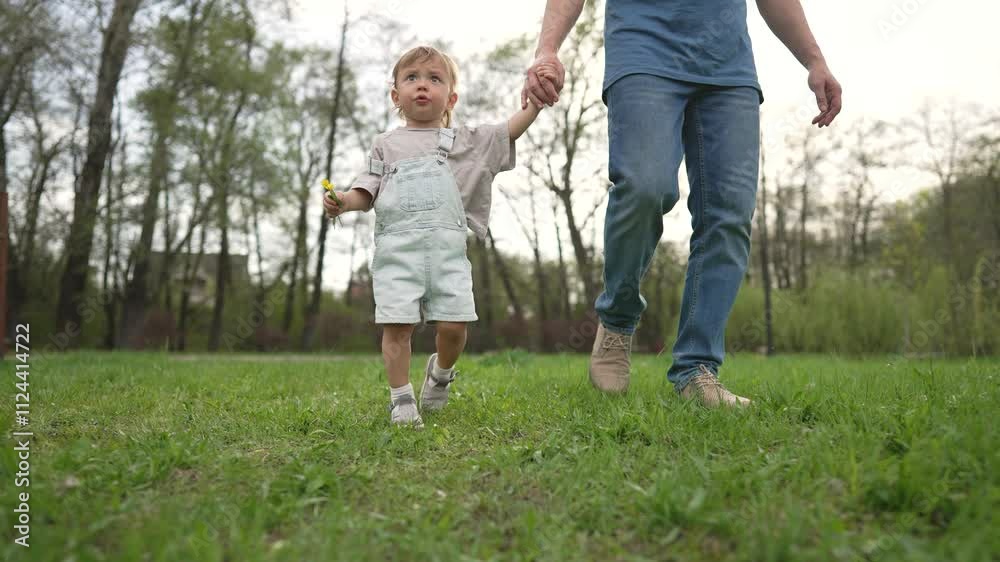 Happy family concept. Dad child walk hand in hand in nature. Family enjoys peaceful walk together exploring nature in park. Child holding flower while walking with dad. Walk family nature outdoor fun. Happy family concept. Dad child walk hand in hand in nature. Family enjoys peaceful walk together exploring nature in park. Child holding flower while walking with dad. Walk family nature outdoor fun.
