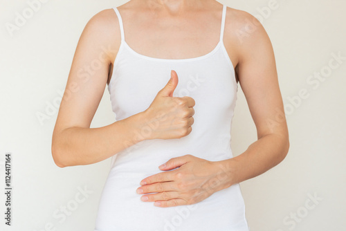 A young Caucasian woman in white clothes, holding her hand on her stomach and giving a thumbs up. The concept of good digestion.