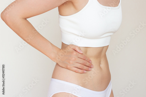 Obraz na płótnie A young woman in white clothes, holding her right side of her stomach with her hand, suffering from liver and gallbladder disease, experiencing acute severe pain