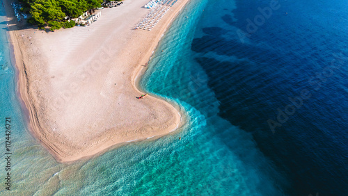 Fototapeta Naklejka Na Ścianę i Meble -  The crystal-clear waters shimmer under the bright sun, while the sandy Zlatni Rat Beach Croatia stretches on Brac Island. Lush greenery frames this picturesque getaway, drone top view of the beach