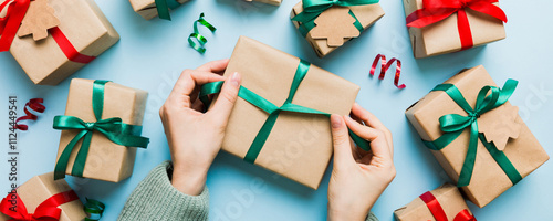 Woman is packing surprise gift for Christmas holidays, sitting at workplace with craft tools, top view. Woman wrapping Christmas gift at colored table photo