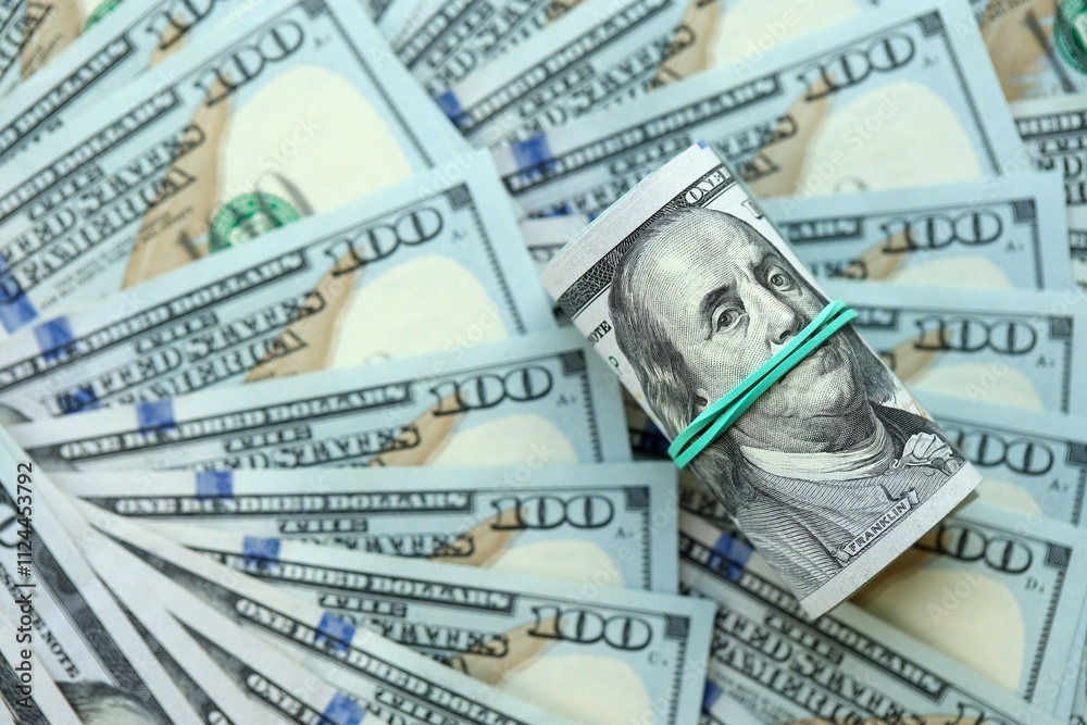 Roll of hundred dollar bills USD banknotes lies on big amount of united states money Roll of hundred dollar bills USD banknotes lies on big amount of united states money