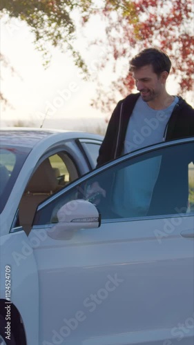 Happy guy gets into car sharing vehicle parked near tree
