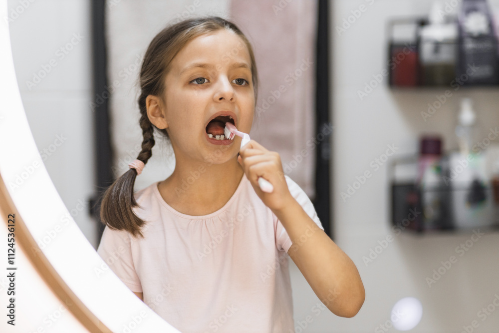 Caucasian girl with missing milk teeth brushing teeth in bathroom. She looks attentively in mirror, focusing on oral hygiene. Concept of childhood routines and dental care. Caucasian girl with missing milk teeth brushing teeth in bathroom. She looks attentively in mirror, focusing on oral hygiene. Concept of childhood routines and dental care.