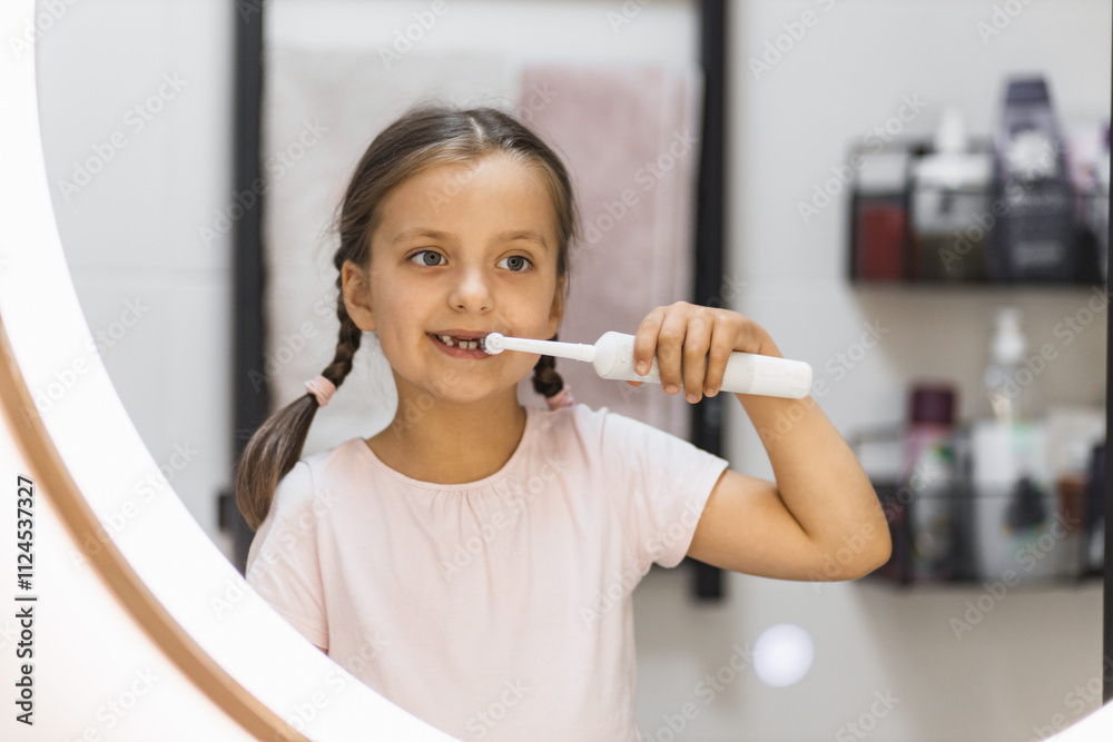 Little Caucasian girl with lost baby teeth using electric toothbrush, looking in bathroom mirror, promoting dental hygiene. Little Caucasian girl with lost baby teeth using electric toothbrush, looking in bathroom mirror, promoting dental hygiene.