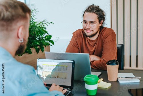 Smiling businessmen sitting with laptops at desk photo