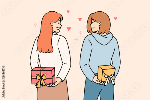 Positive girls hold gifts boxes behind their backs and look at each other lovingly, showing sympathy and affection. Young casual women exchange gifts on eve of march 8 or valentine day.