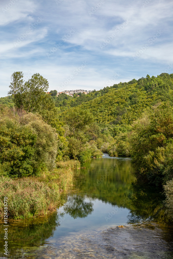 Scenic view of the Cetina River in Dalmatia, Croatia, surrounded by lush greenery and hills, under a partly cloudy sky. Scenic view of the Cetina River in Dalmatia, Croatia, surrounded by lush greenery and hills, under a partly cloudy sky.
