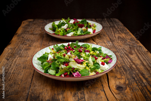 Mixed green salad with feta and pomegranate seeds on a rustic wooden table photo