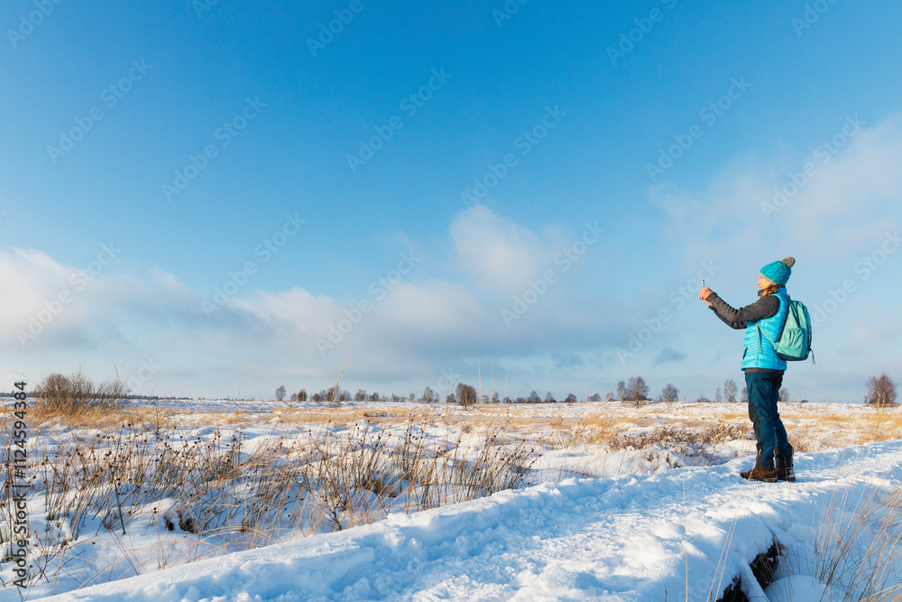 Senior woman taking smartphone photos in snowy High Fens nature park in Belgium Senior woman taking smartphone photos in snowy High Fens nature park in Belgium