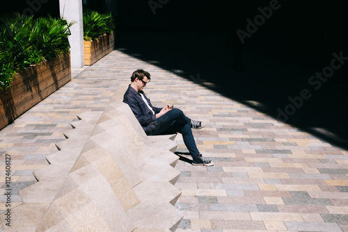 Man using smart phone sitting on sunny day photo