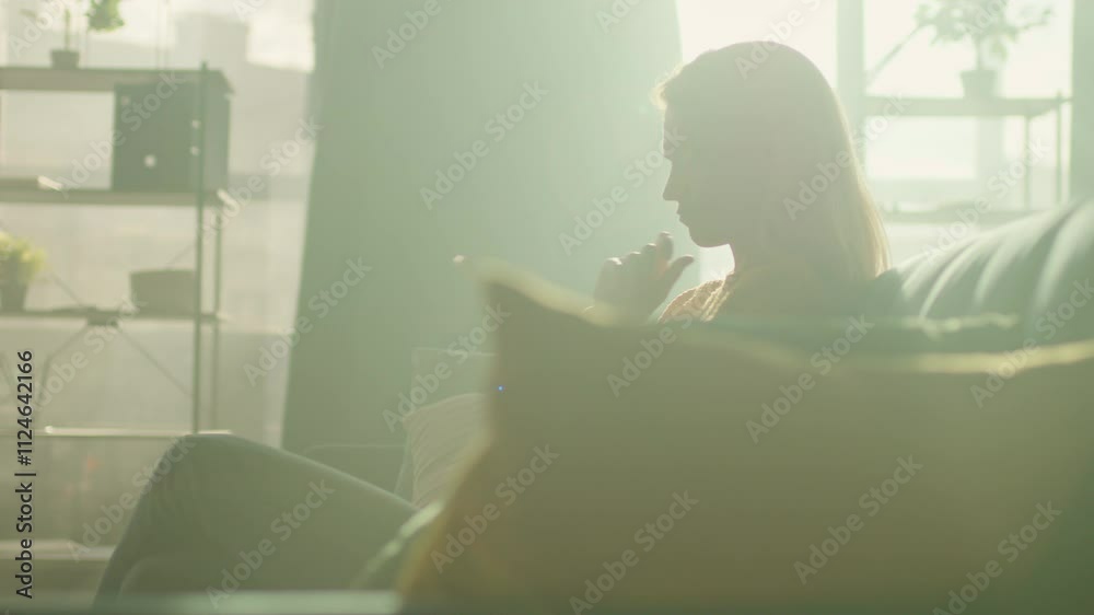 Sad woman sitting of the sofa at home using phone thinking. Sunlight in room. Camera moving around. 360 degrees