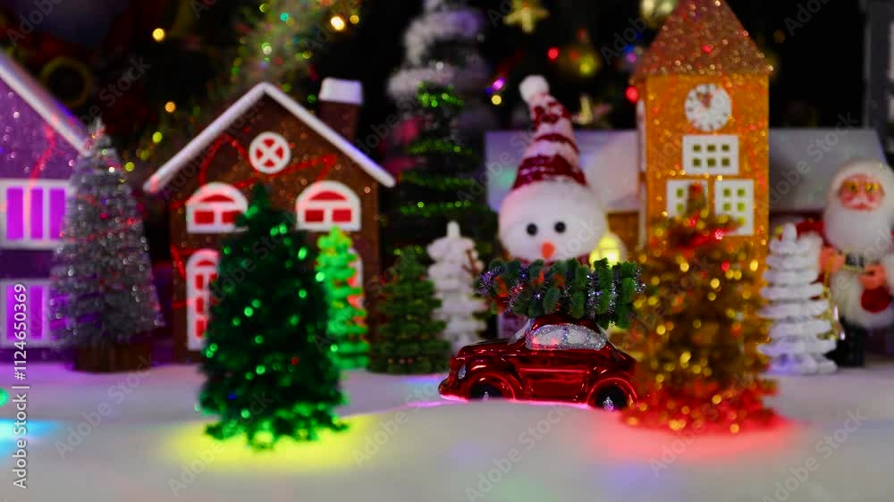 A small red car with a Christmas tree on the roof moves through the middle of a Christmas town A small red car with a Christmas tree on the roof moves through the middle of a Christmas town