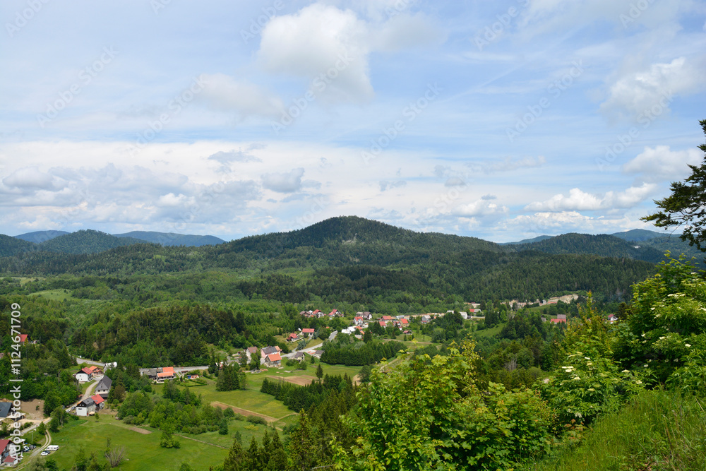 Fototapeta premium A view towards the municipality of Lokve as seen from a lookout point on the road above Lokve Lake (Lokvarsko jezero) in Croatia, featuring lush forests and picturesque village scenery